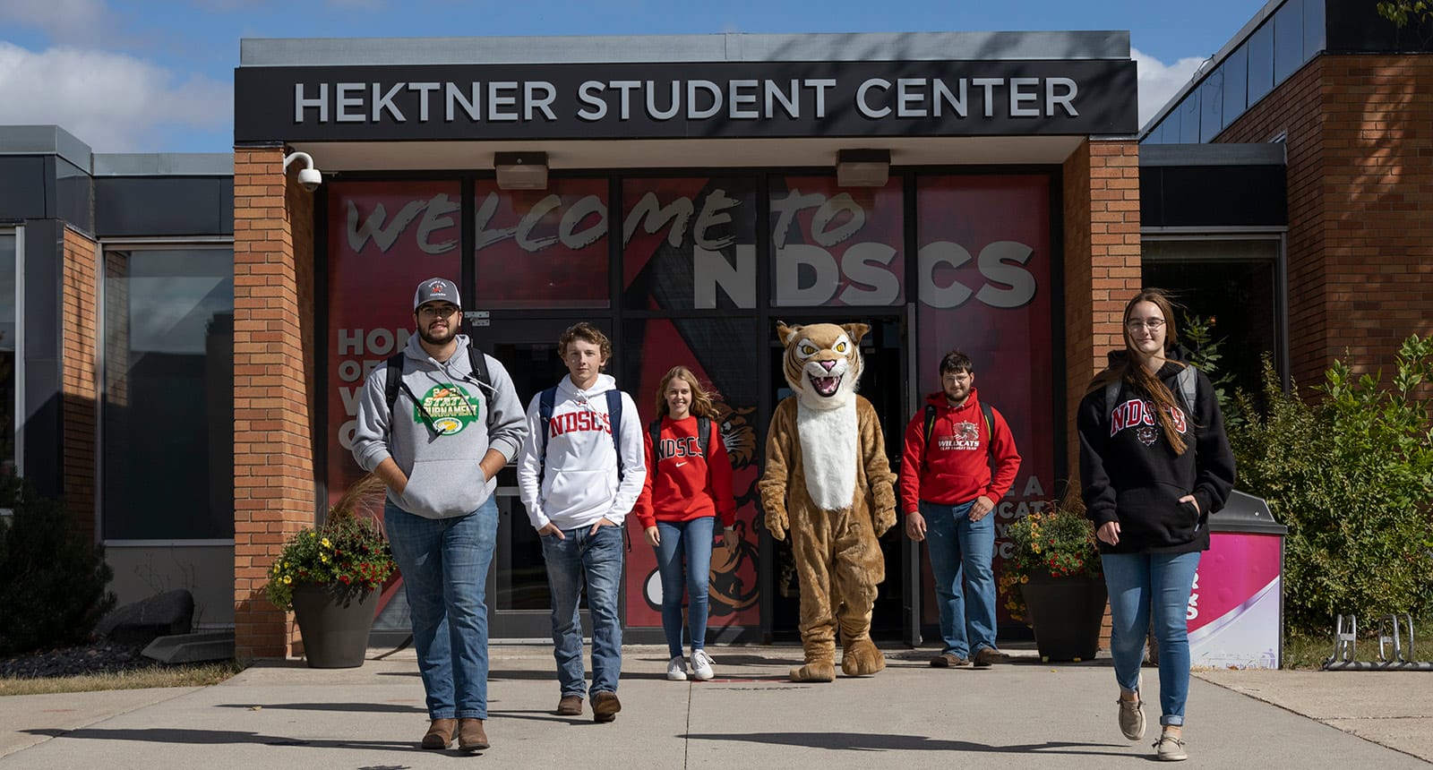 Group of NDSCS students and mascot walking out of the Hektner Student Center on a sunny day.