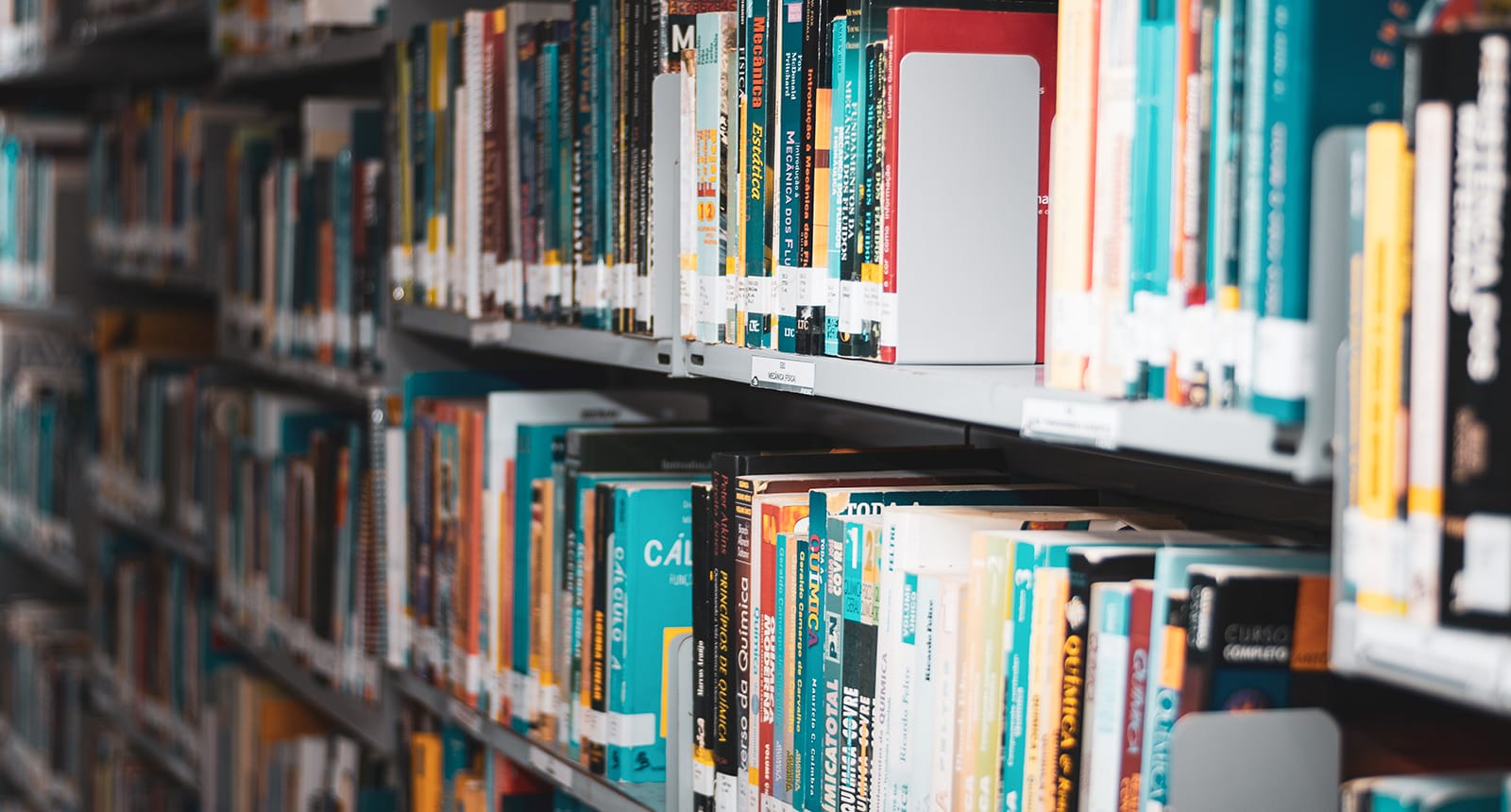 Close-up view of books lined up on multiple shelves in a library aisle, with colorful spines and labels visible.
