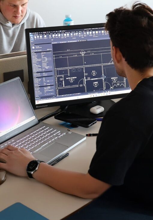 Student working at a dual-monitor setup, using architectural drafting software to design a residential floor plan.