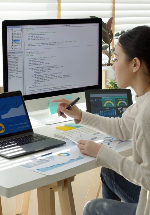 Woman analyzing financial reports at a desk with multiple screens showing data dashboards, charts, and code.
