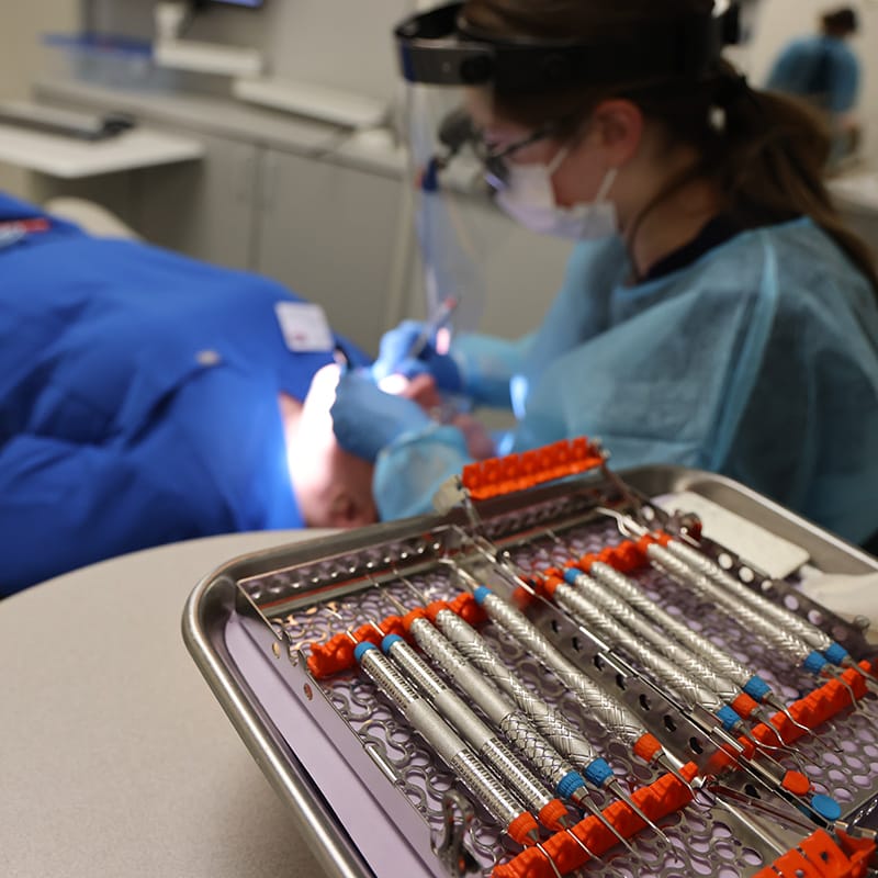Close-up of dental tools on a tray with a hygienist working on a patient in the background.