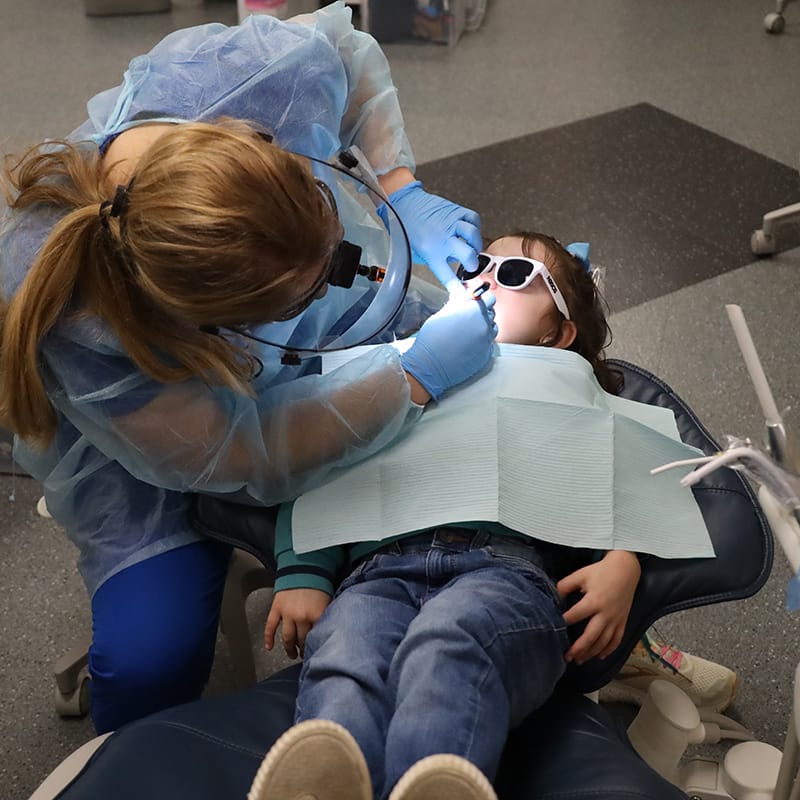 Dental hygienist examining a young child wearing sunglasses during a dental checkup.