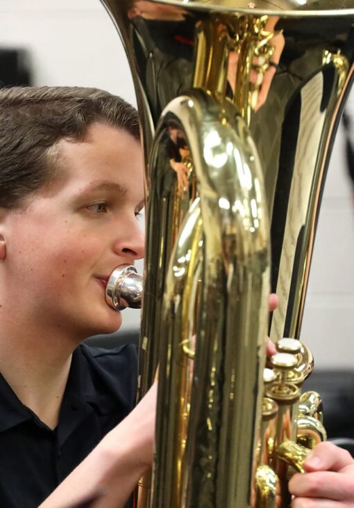 Student playing a brass instrument in a music rehearsal room, focused on performance.