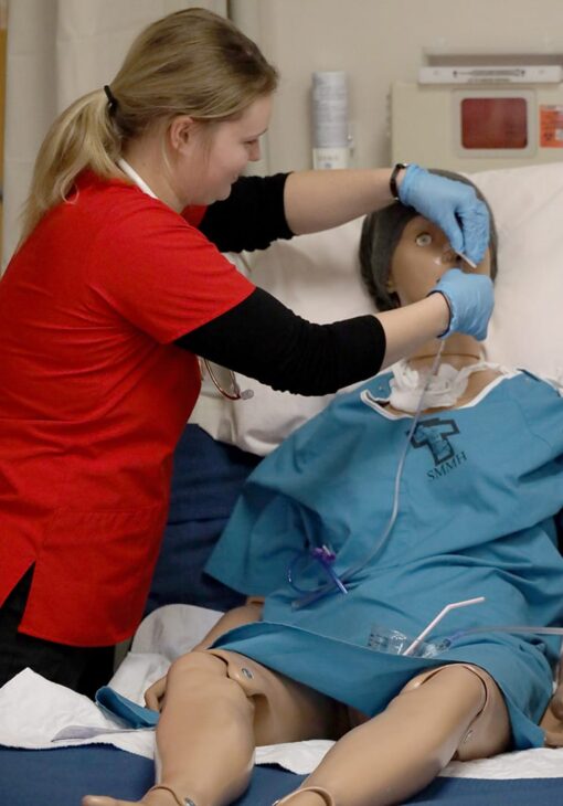 Nursing student inserting a tube into a training mannequin’s nose during a clinical simulation.