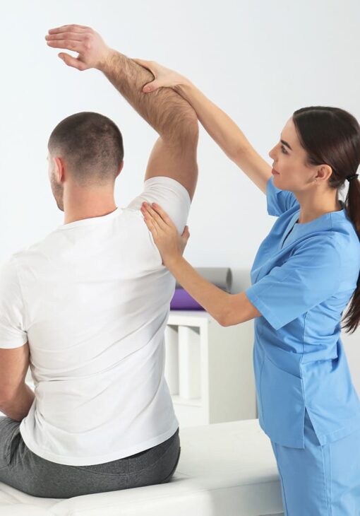 Female physical therapist in blue scrubs assisting a male patient with arm mobility exercises during a rehabilitation session.