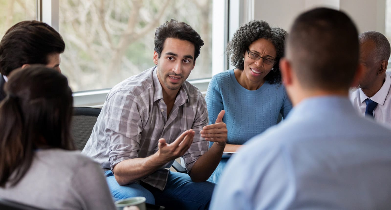 Man speaking to a small group during a discussion in a bright meeting room.