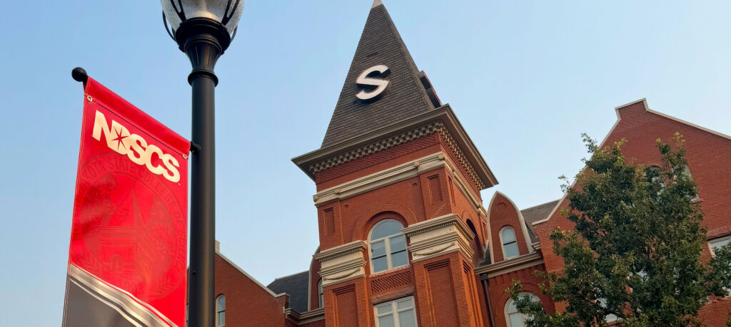 Close up of Old Main steeple and lamp post with a red, black, and white NDSCS banner