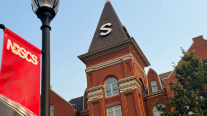 Close up of Old Main steeple and lamp post with a red, black, and white NDSCS banner