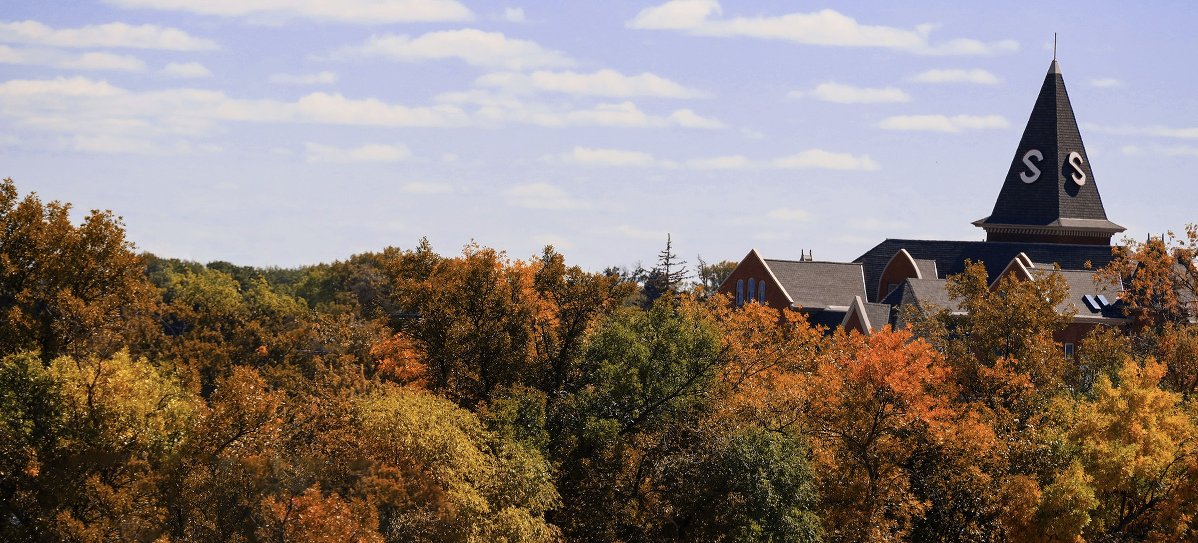 Old Main steeple peaks above orange, yellow, green, and brown autumn foliage